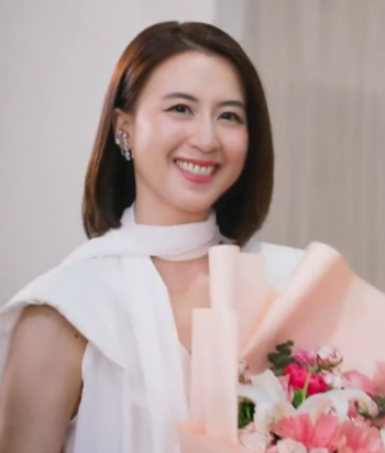 Smiling woman in white clothing holds a large pink flower bouquet toward the camera.