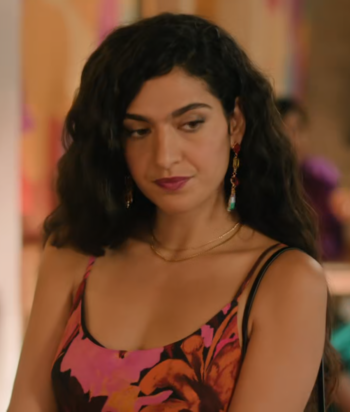 Woman with dark wavy hair in a colorful floral dress, looking to her left, wearing dangling earrings.