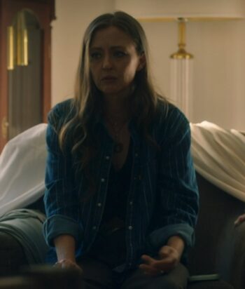 Woman with long hair in a blue striped shirt sits on a sofa, looking distressed in a living room.