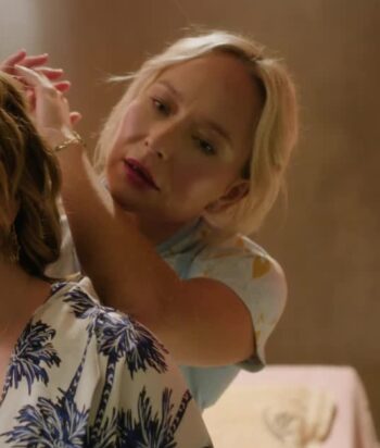 Woman with blonde hair helping another woman adjust her hair or clothing, close-up in soft lighting.
