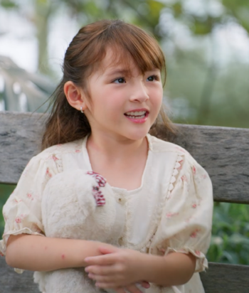 Young girl with brown hair sits on a wooden bench outdoors, holding a white plush bunny.