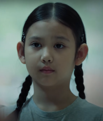 Close-up of a young girl with two braids looking slightly to the left, neutral expression.