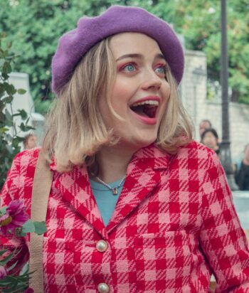 Smiling woman wearing a purple beret and pink patterned cardigan outdoors, with flowers in the foreground and greenery behind her.