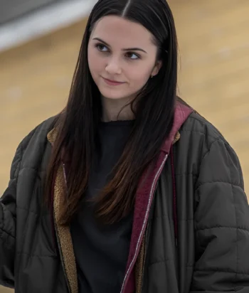 Young woman with long dark hair wearing a black top and a dark green quilted jacket, looking to the side outdoors.