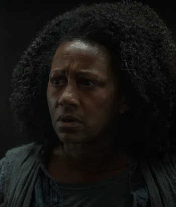 CarlaMcLain – LezWatch.TV Close-up of a worried Black woman with curly hair looking to the side in a dimly lit scene.