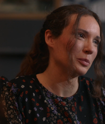 Portrait of a woman with brown hair in a floral black dress, looking to the right in a thoughtful moment.