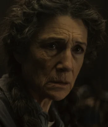 Close-up of an elderly woman's face with deep wrinkles, looking pensively to the side in dim lighting.