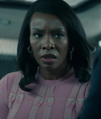 Concerned woman in a pink sweater sits in a vehicle, looking to the side with a serious expression. oriented indoors, partial view of a seat behind her.