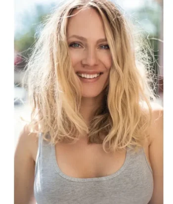 019c5f98-096e-2452-03a9-72649bfd28cf_2217ab_cropped – LezWatch.TV Smiling woman with shoulder-length blonde hair wearing a gray tank top outdoors on a sunny day.
