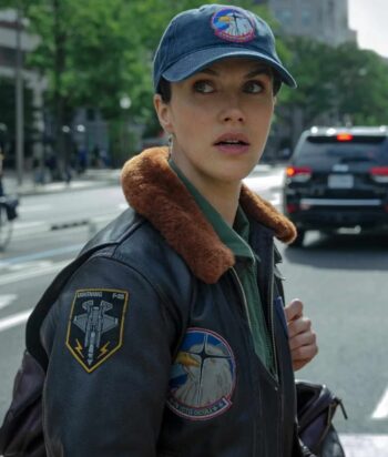 Woman wearing a dark leather jacket with a brown fur collar and space/jet patches, looking over her shoulder on a city street.