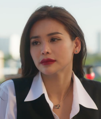 Night – LezWatch.TV Close-up of a woman with dark hair and red lipstick wearing a white collared shirt and black vest, outdoors.