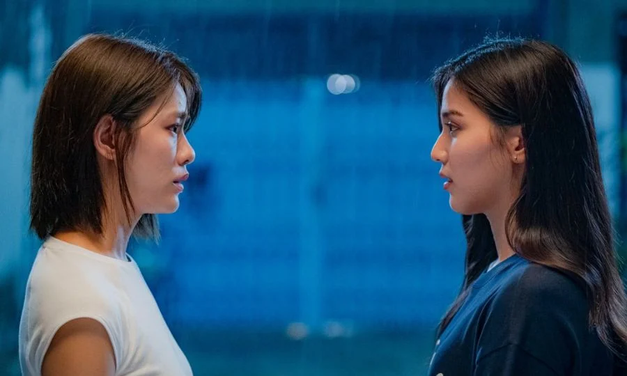 Two women in profile facing each other, talking in a blue-lit space.