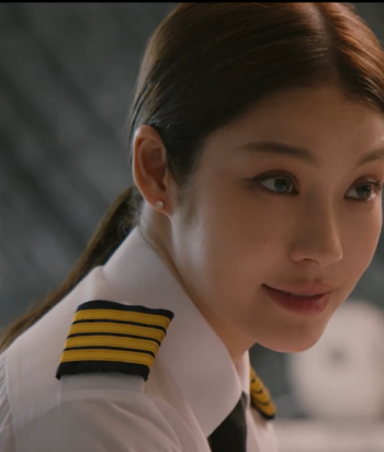 Portrait of a smiling female airline pilot in a white uniform shirt with gold-striped epaulets, hair tied back.
