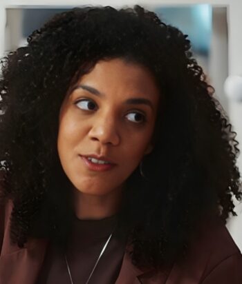 Woman with curly hair in a brown blazer looking to her left indoors.