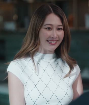 Smiling woman with long hair in a white studded top, facing someone off-camera in an indoor setting.