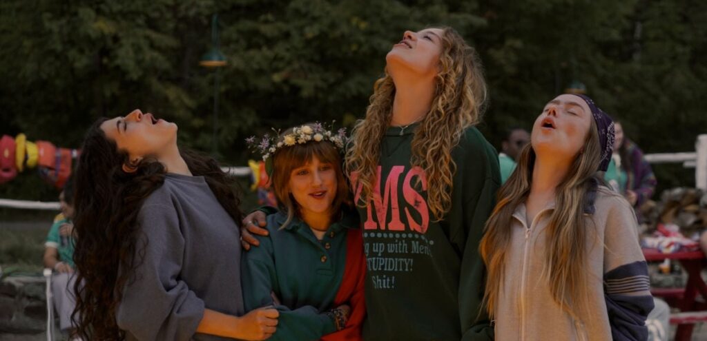 Four young women standing outdoors, looking up with smiles and arms around each other