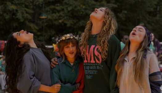 Four young women standing outdoors, looking up with smiles and arms around each other