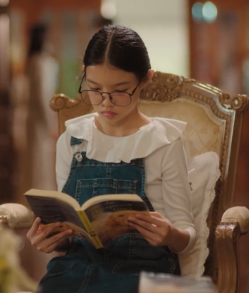 Girl with glasses reading a book while seated in an ornate wooden armchair.