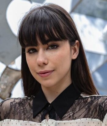 Close-up portrait of a woman with dark hair and bangs wearing a black-collared lace blouse.